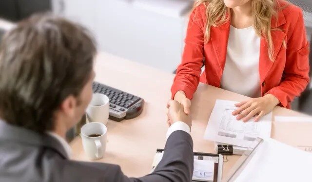 A man and woman shaking hands over papers.