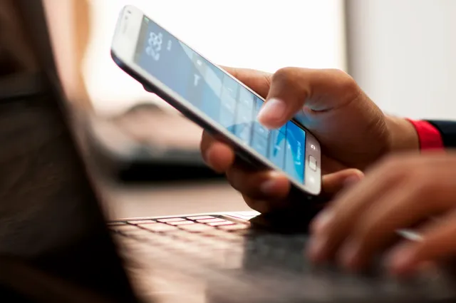 A person is using their phone while sitting at the computer.